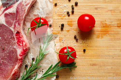 Image of Pieces of crude meat with rosemary and tomatoes.