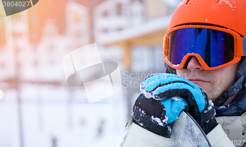 Image of Man snowboarder wearing orange helmet, grey jacket, black and blue gloves standing with snowboard