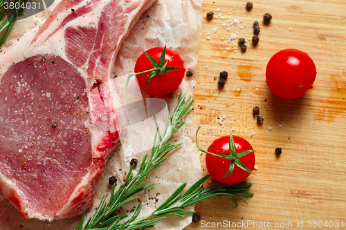 Image of Pieces of crude meat with rosemary and tomatoes.