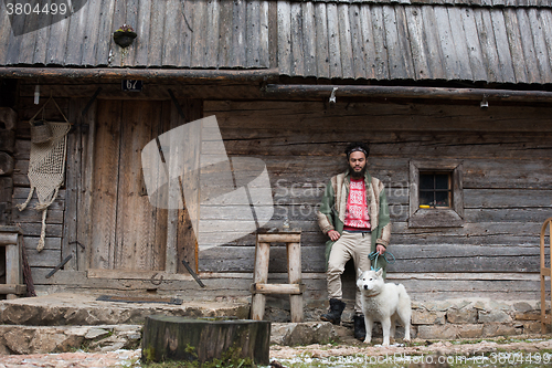 Image of hipster with dog in front of wooden house