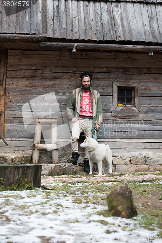 Image of hipster with dog in front of wooden house