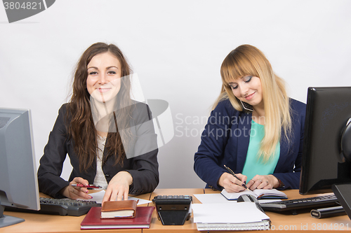 Image of  Young girls in the office, one looks in the frame, the second talking on the phone and writing in diary
