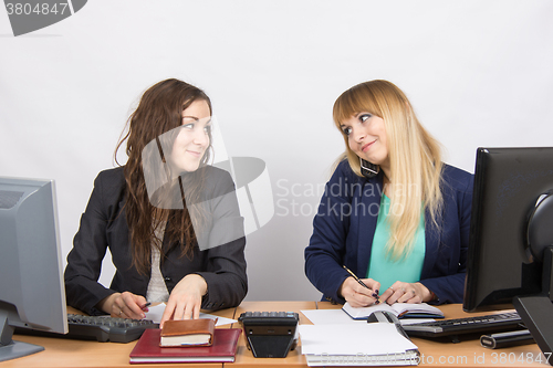 Image of Young girls in the office looked at each other, one of them talking on the phone and writing in a notebook