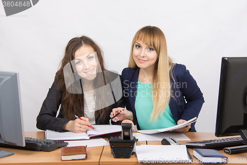 Image of Two girls colleagues together looking office documents and looked into the frame
