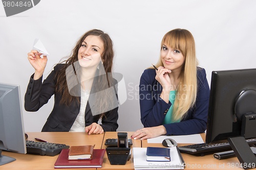 Image of Two young women working in the office, one made a paper plane, the second stares into the frame