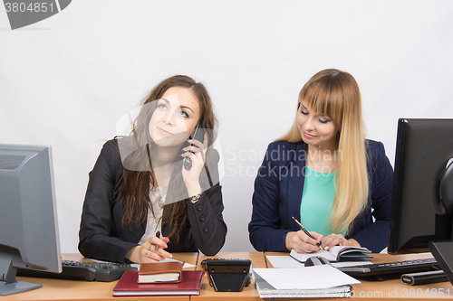 Image of Young girls in the office, another talking on the phone, the other writes in diary