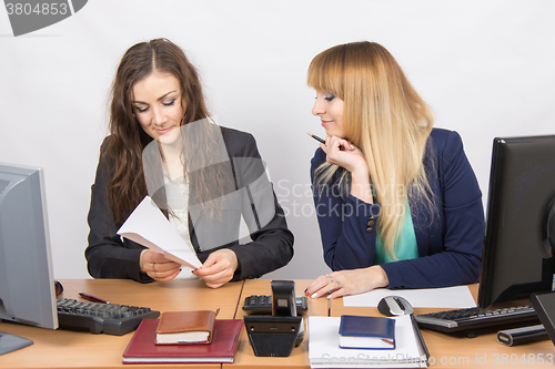 Image of Two young girls working in an office, making a paper airplane, and the second looks at her in surprise