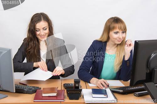 Image of Two young women working in the office, one of fun took a sheet of paper, the second looks at the computer screen
