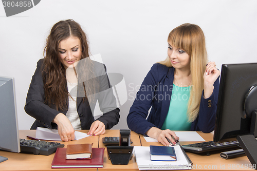 Image of Two young women working in the office, one puts a piece of paper, the second in amazement staring at her