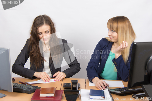 Image of Two young girls working in an office, making a paper airplane, and the second with hatred looks at her