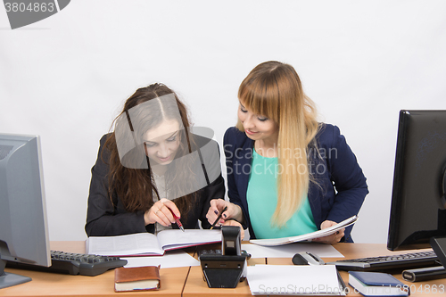 Image of Two girls are looking for colleagues sitting together the right information at the same table in the office