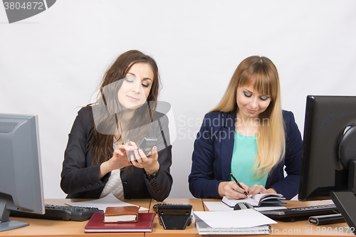 Image of Young girls in the office, one dials a phone number, the second writes in diary