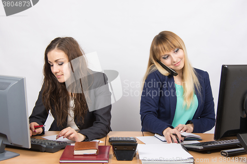 Image of Young girls in the office, one works in the computer, the other on the phone and looking at the screen