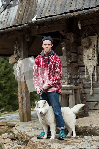 Image of young hipster with dog in front of wooden house