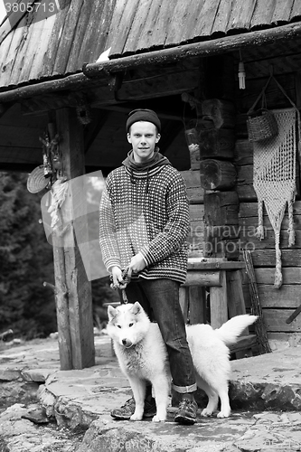 Image of young hipster with dog in front of wooden house
