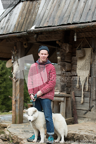 Image of young hipster with dog in front of wooden house