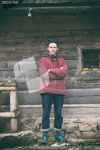 Image of young hipster in front of wooden house