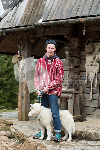 Image of young hipster with dog in front of wooden house