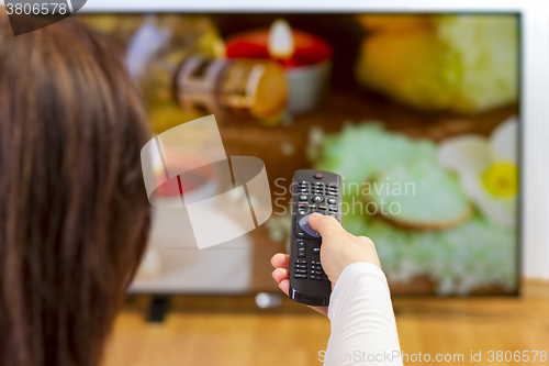 Image of Young woman sitting on sofa holding tv remote and surfing progra