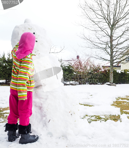 Image of Girl making snowman in garden, hiding under pink hat