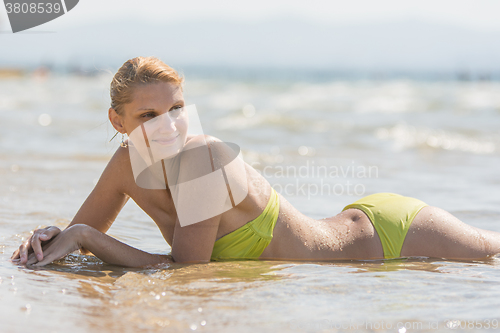 Image of Young beautiful girl lying on her stomach in the water on the sandy sea beach