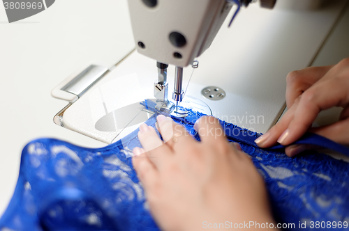 Image of Hands of a woman sewing blue fabric