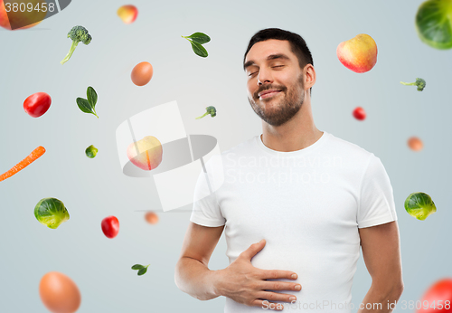 Image of happy full man touching tummy over falling fruits