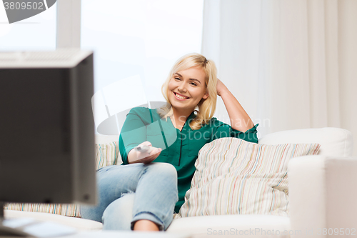 Image of smiling woman with remote watching tv at home