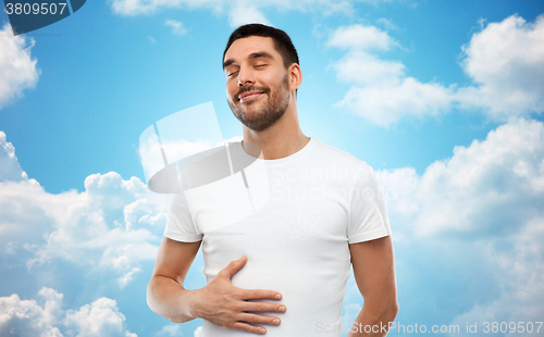 Image of happy full man touching tummy over blue sky