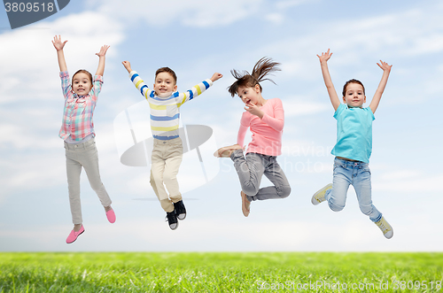 Image of happy children jumping in air over sky and grass