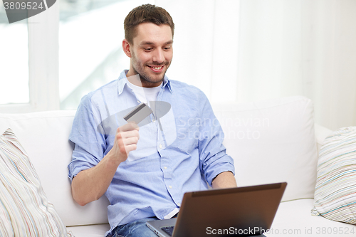 Image of smiling man with laptop and credit card at home