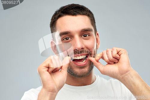 Image of man with dental floss cleaning teeth over gray