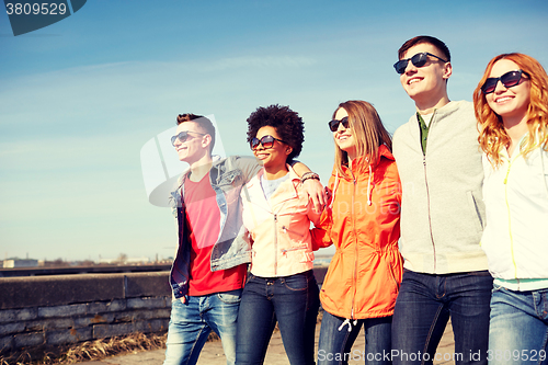 Image of happy teenage friends walking along city street