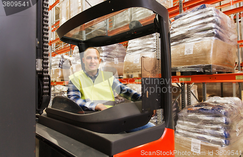 Image of smiling man operating forklift loader at warehouse