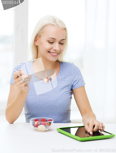 Image of smiling woman eating fruits with tablet pc at home