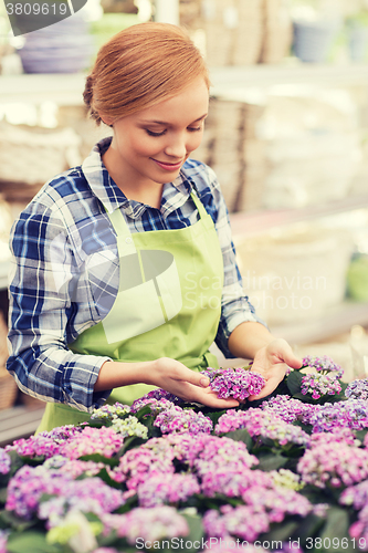 Image of happy woman taking care of flowers in greenhouse