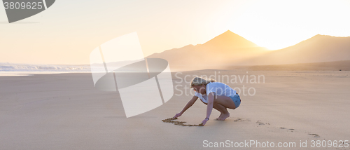 Image of Lady drawing heart shape in sand on beach.