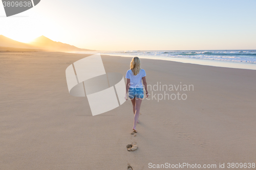 Image of Lady walking on sandy beach in sunset leaving footprints behind.