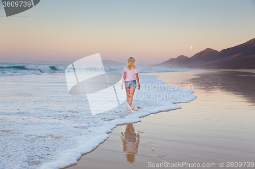 Image of Lady walking on sandy beach in sunset.