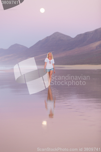 Image of Lady walking on sandy beach in sunset.