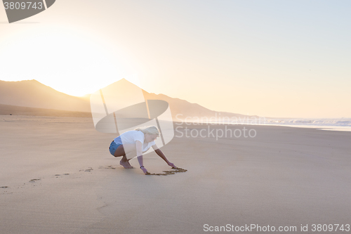 Image of Lady drawing heart shape in sand on beach.