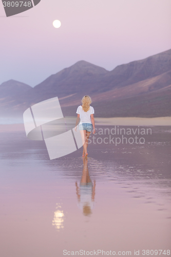 Image of Lady walking on sandy beach in sunset.