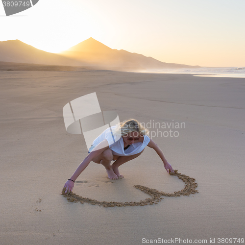 Image of Lady drawing heart shape in sand on beach.