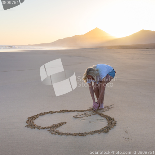 Image of Lady drawing heart shape in sand on beach.