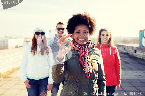 Image of happy teenage friends showing ok sign on street