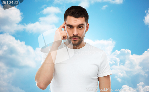 Image of man with finger at temple over blue sky background