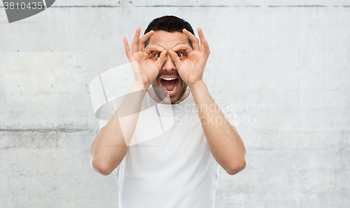 Image of man making finger glasses over gray background