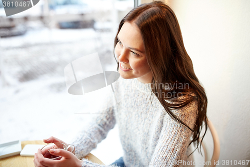 Image of smiling young woman drinking tea at cafe