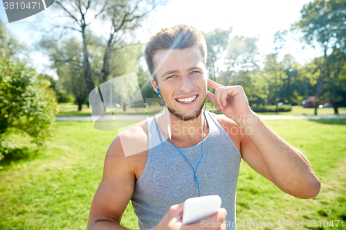 Image of happy man with earphones and smartphone at park