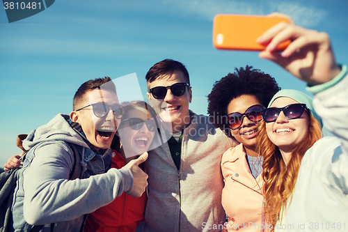 Image of smiling friends taking selfie with smartphone